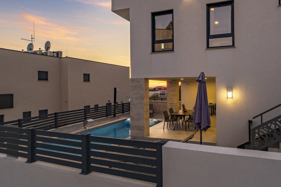 The house and pool at dusk, the dining area lit
